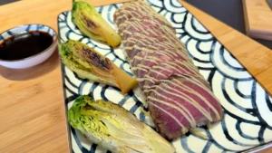 Le plat final avec le tataki de bœuf tranché sur un lit de riz vinaigré, garni de sucrines grillées et d'une mayonnaise au wasabi. Le plan est stable et bien éclairé, mettant en valeur la présentation.