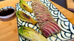 Le plat final avec le tataki de bœuf tranché sur un lit de riz vinaigré, garni de sucrines grillées et d'une mayonnaise au wasabi. Le plan est stable et bien éclairé, mettant en valeur la présentation.