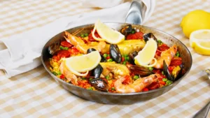 gros plan sur la paella dressée dans sa poêle avec crevettes, moules, poulet et citrons